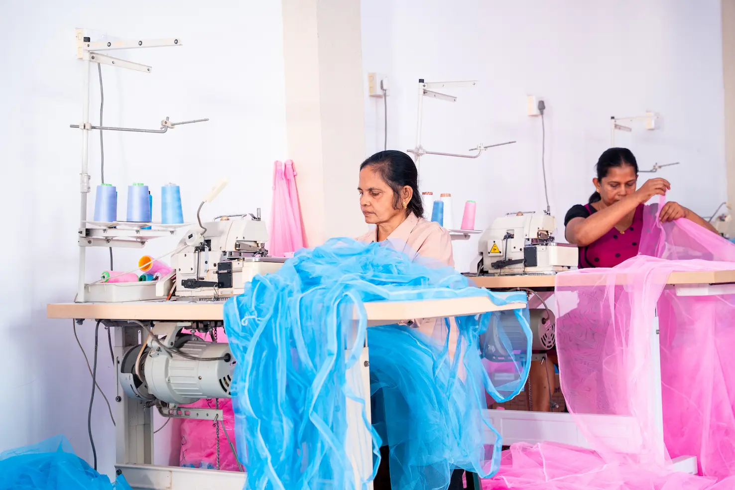 Two machinists finishing blue and pink mosquito netting at overlocking machines